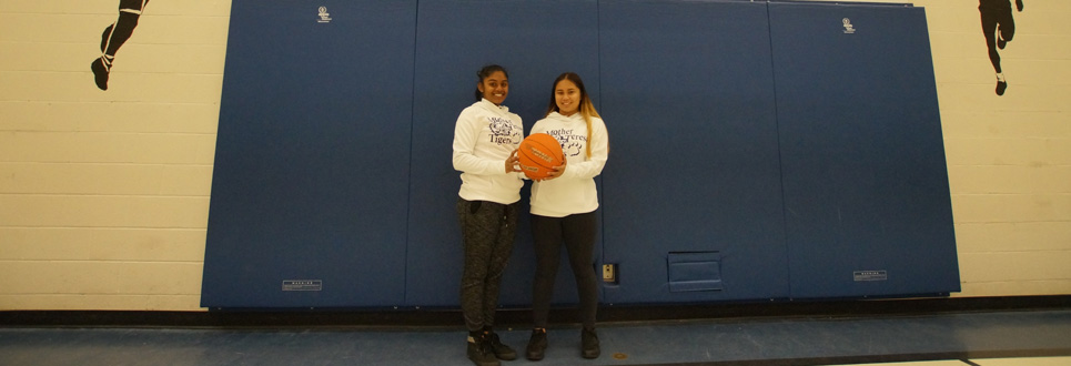 Two students wearing sports uniforms, holding a basketball.